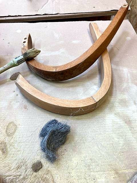 Bois cintrés d'un fauteuil, pinceau et laine d'acier posés sur un drap d'atelier